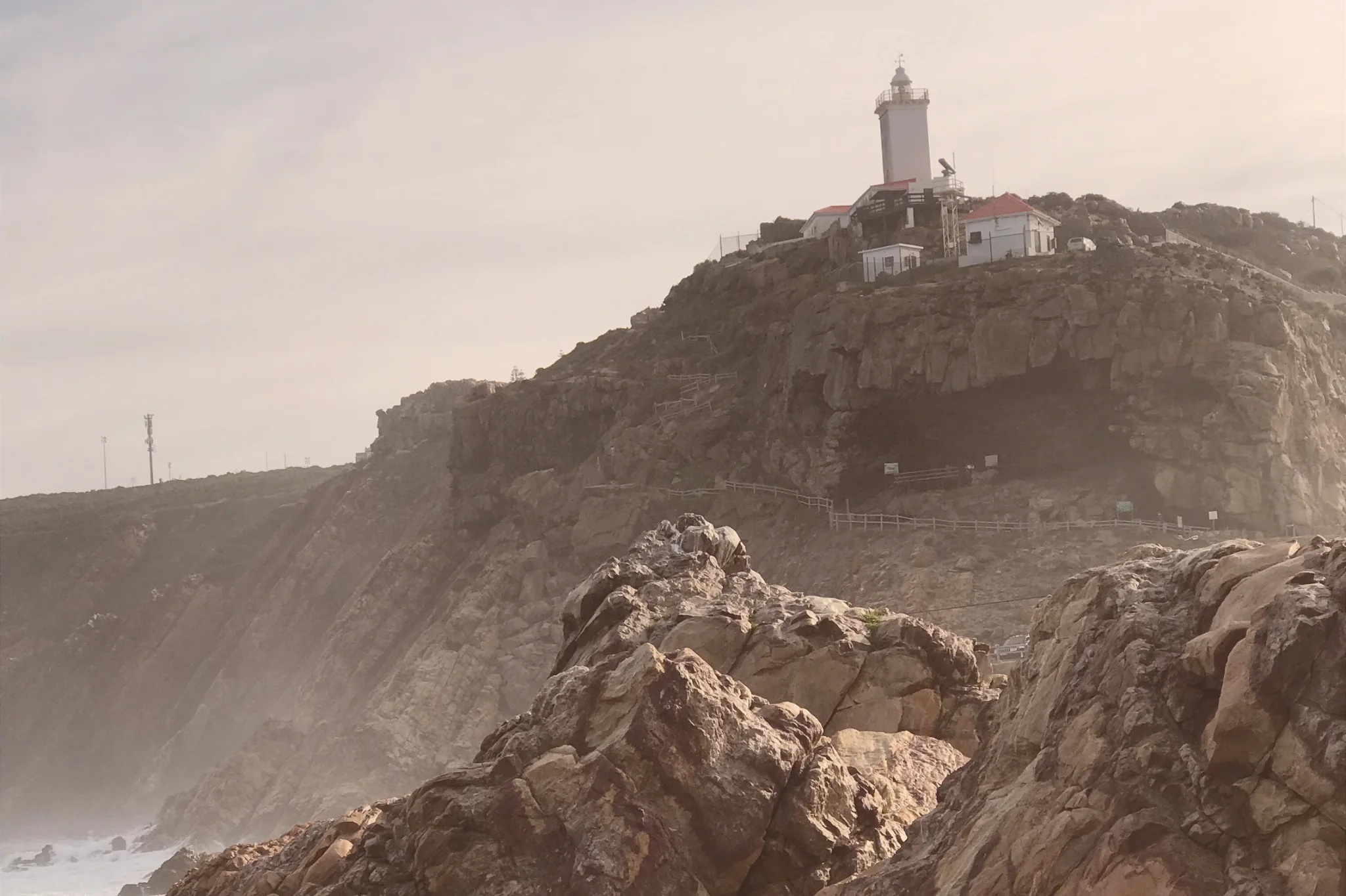 Cape St Blaize Lighthouse stands above rugged coastal cliffs in Mossel Bay, with the broad entrance to Cape St Blaize Cave visible below.