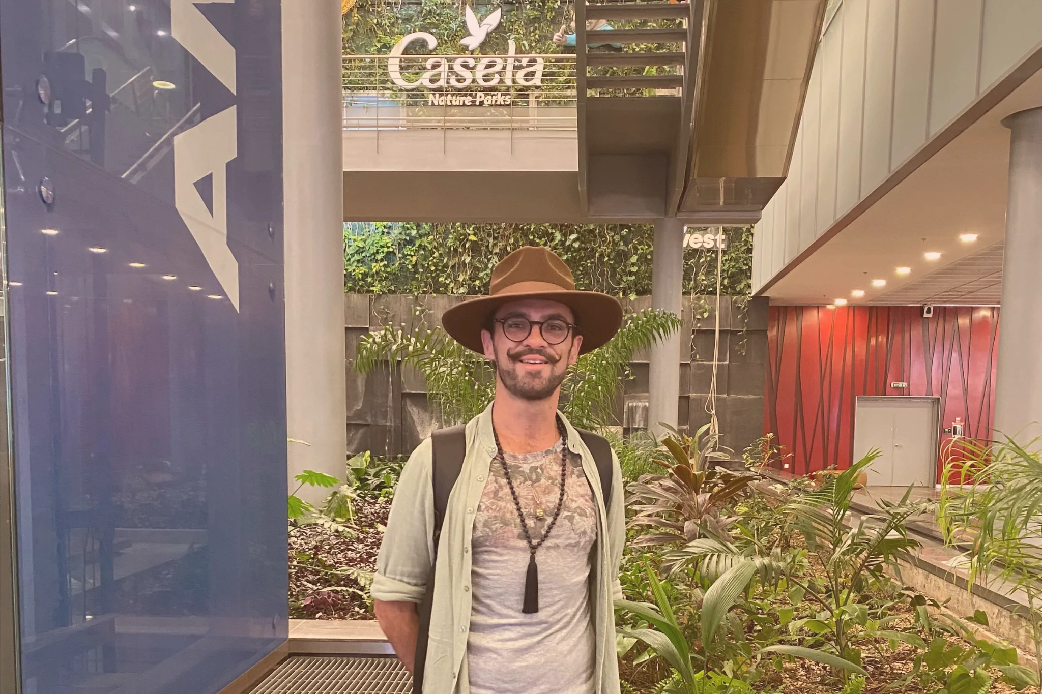 A traveller in a brown wide-brimmed hat stands beside tropical plants inside Sir Seewoosagur Ramgoolam International Airport in Mauritius.