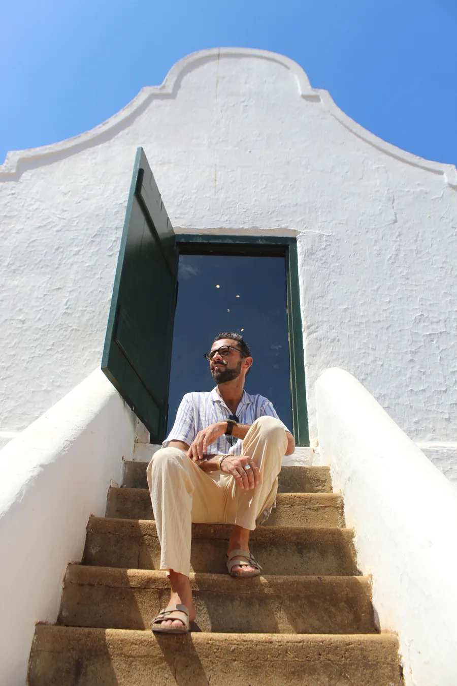Mikhail seated on stone steps outside a whitewashed Cape Dutch Farmhouse building at Babylonstoren Farm Estate, Cape Winelands District.
